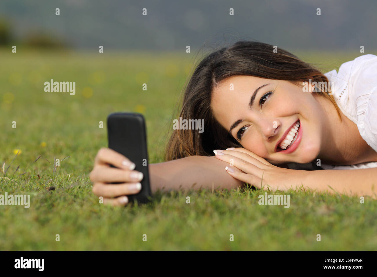 Pretty girl smiling en utilisant un téléphone intelligent couché dans l'herbe dans un parc ou d'une montagne Banque D'Images