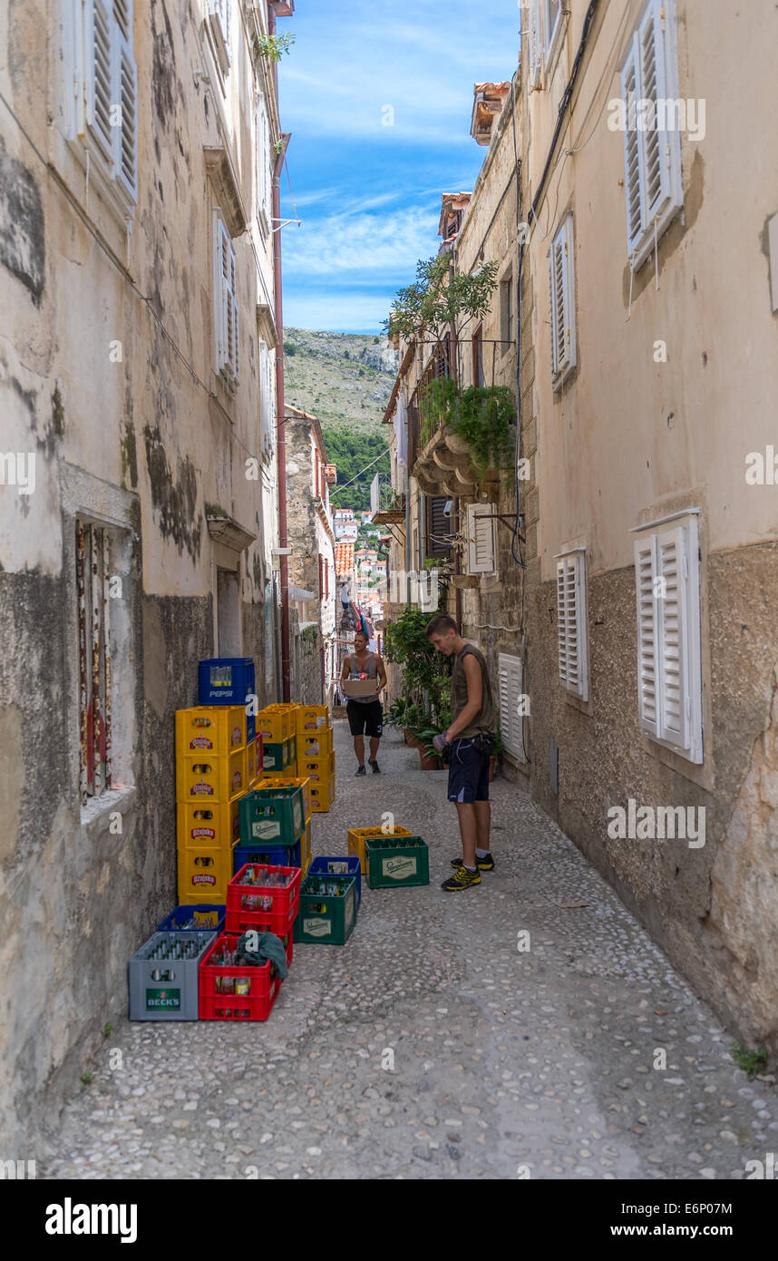 Deux jeunes hommes transporter et empiler des caisses de bière en bouteille dans une rue dans la vieille ville de Dubrovnik. Banque D'Images