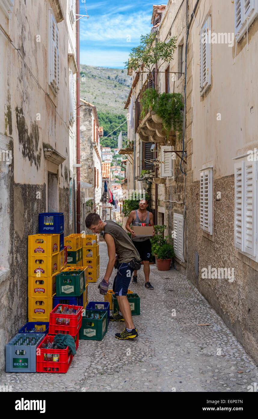 Deux jeunes hommes transporter et empiler des caisses de bière en bouteille dans une rue dans la vieille ville de Dubrovnik. Banque D'Images