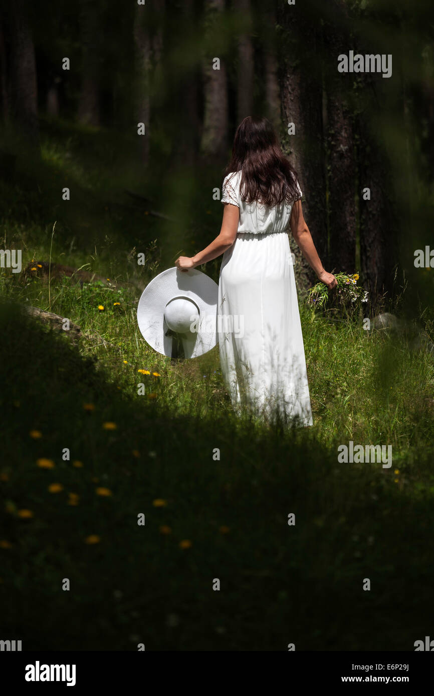 Femme en robe blanche de derrière la tenue d'un chapeau de marcher dans une forêt Banque D'Images
