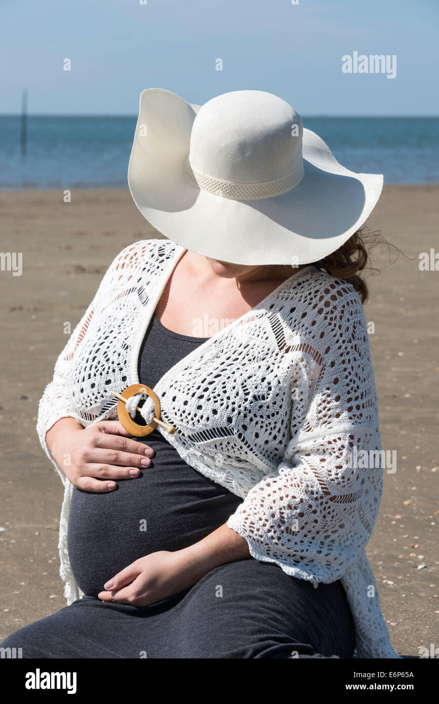 Des profils pregnant woman holding ses mains sur son ventre sur la plage avec du sable et de la mer Banque D'Images