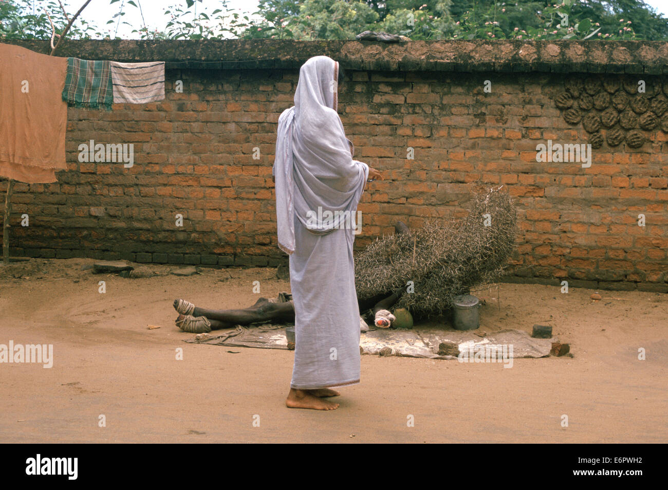 Une femme est l'aumône à un lépreux. Le lépreux est allongé sur le sol avec un buisson sur son corps (Inde) Banque D'Images