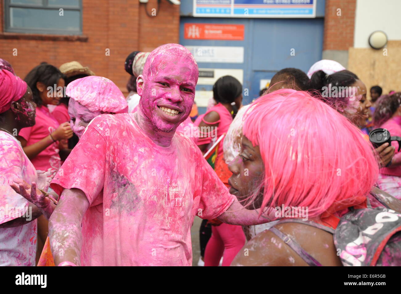 Jeune homme noir à Notting Hill Carnival couvert de peinture rose smiling for the camera Banque D'Images