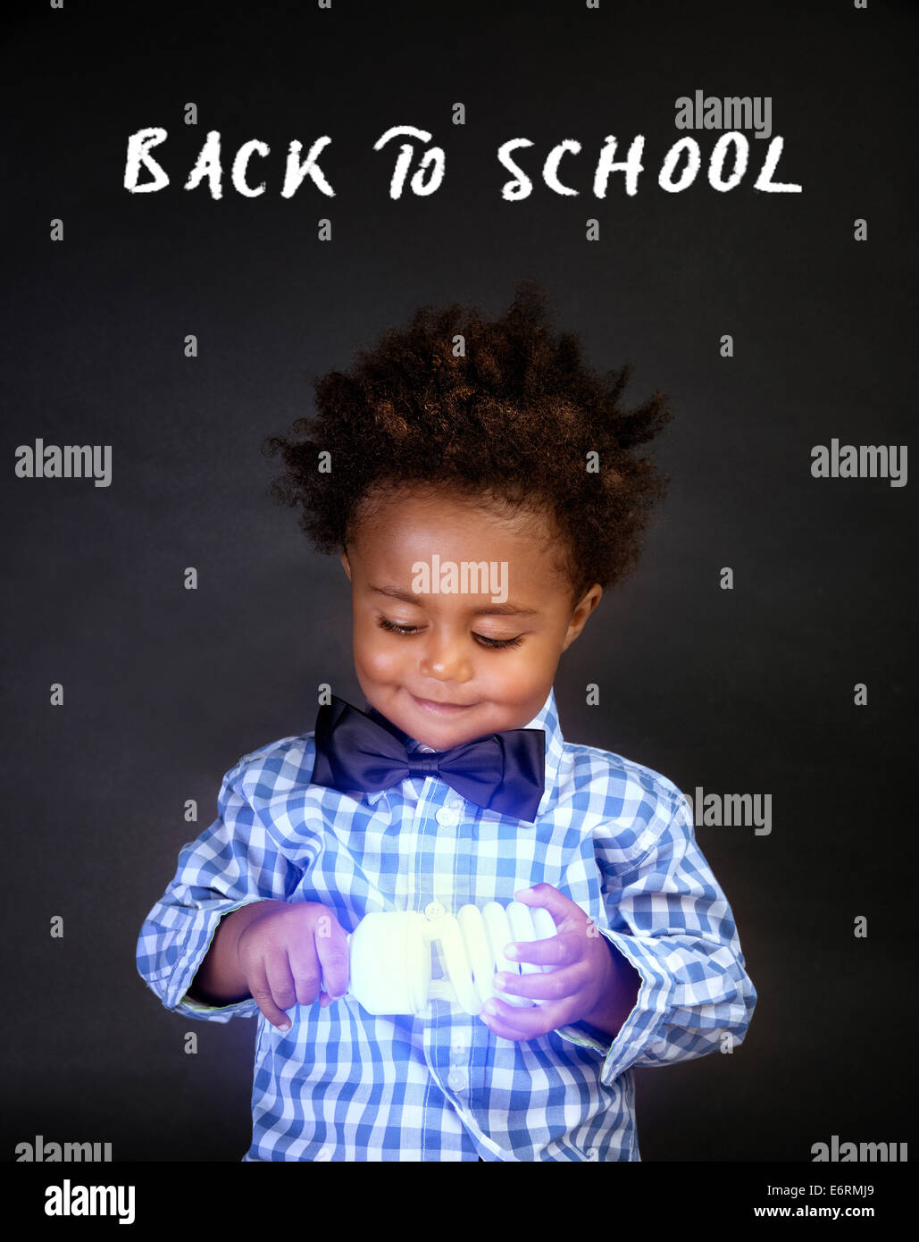 Smart little boy holding en mains lampe électrique lumineux isolé sur fond noir, de l'innovation en physique, le retour à l'école Banque D'Images