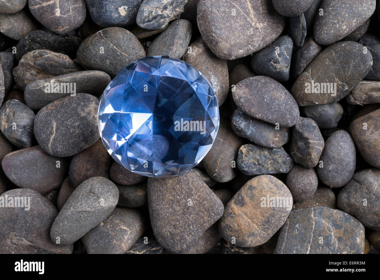 Verre en forme de diamant sculpté entre les cailloux noirs Banque D'Images