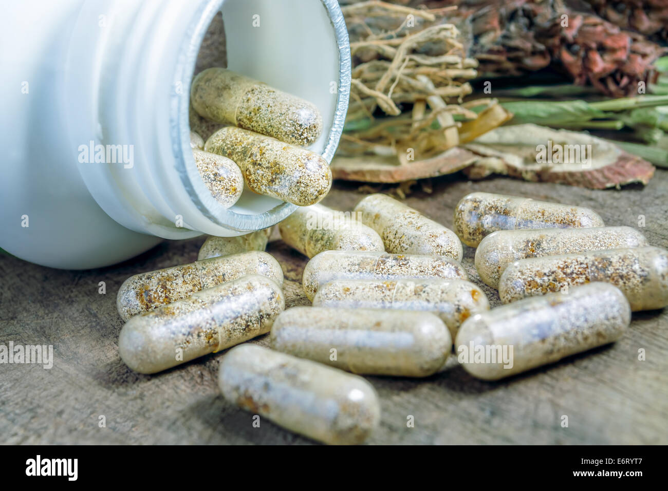 La médecine de fines herbes chinoise traditionnelle de remplacement sur capsule allongée sur une table en bois avec un peu de contexte sur l'herbe Banque D'Images