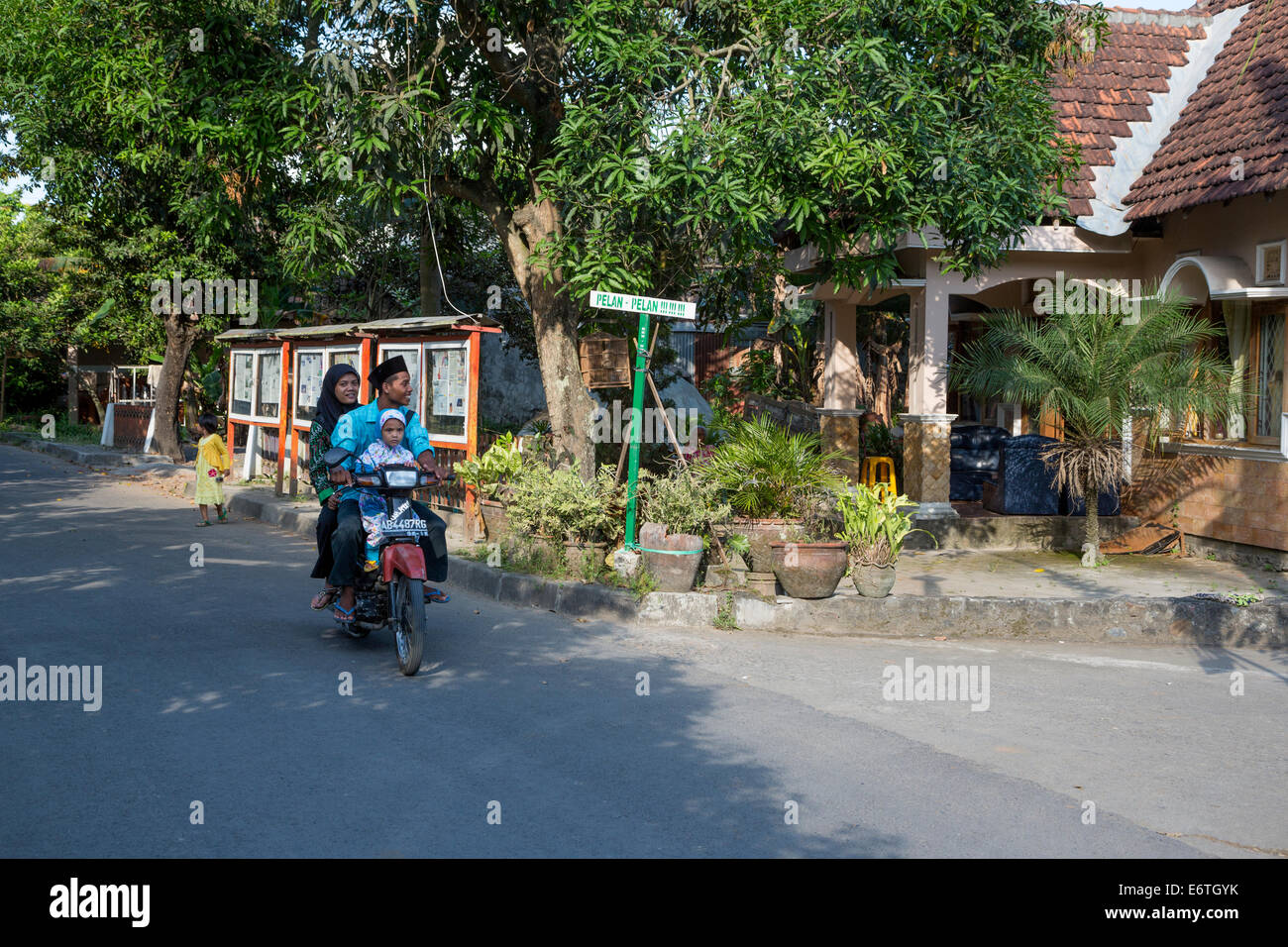 Yogyakarta, Java, Indonésie. La famille sur une moto journal qui passe sur l'affichage dans une zone résidentielle. Banque D'Images