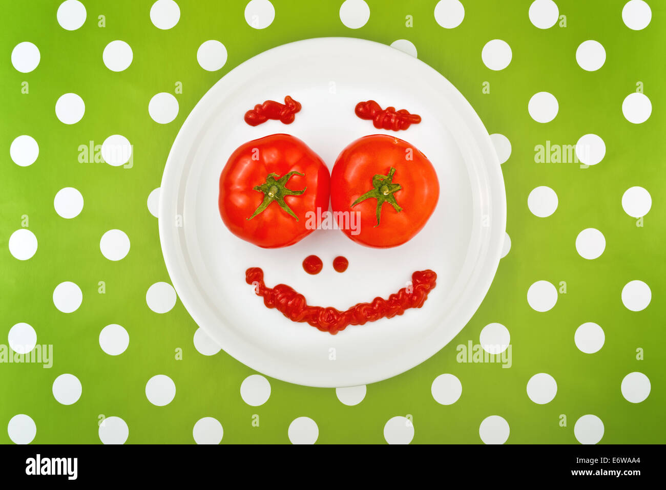 Tomates rouges mûres et ketchup faire smiley émoticone visage servi sur une plaque blanche sur table. Banque D'Images