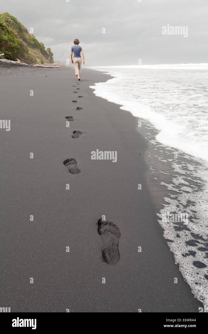 Des empreintes de pas dans le sable noir, femme marchant le long de la plage, l'île du Sud, Nouvelle-Zélande Banque D'Images