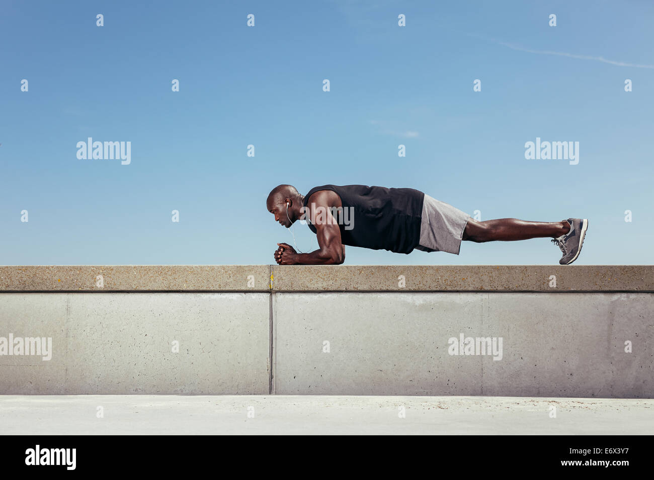 Vue latérale d'une jeune athlète africain faisant exercice de base sur un mur par une passerelle. La jeune athlète exercising outdoors Banque D'Images