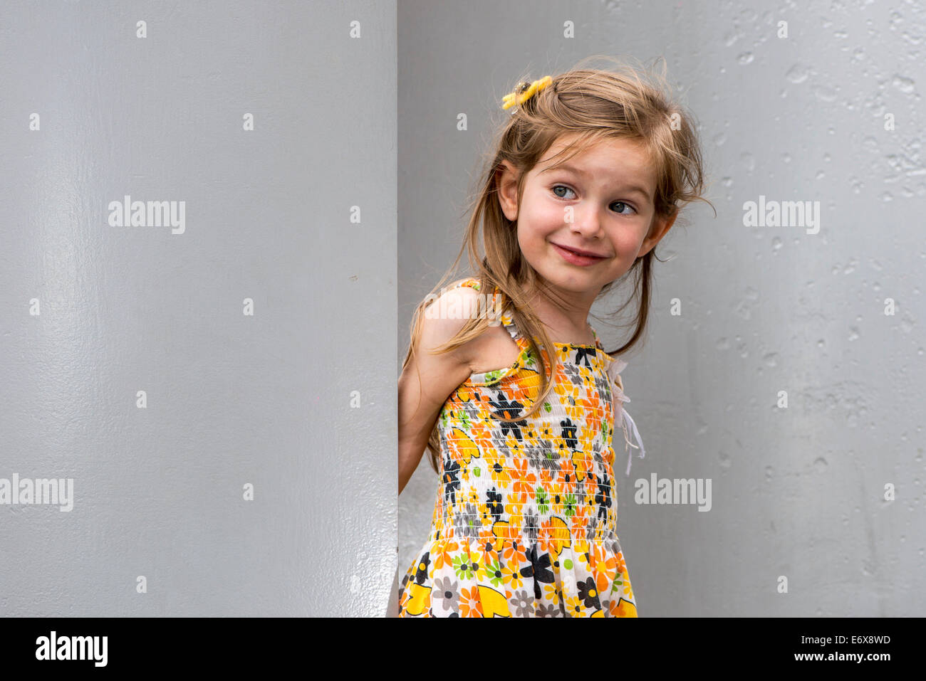 A smiling girl, 3 ans, porte une robe, debout entre les murs, Allemagne Banque D'Images