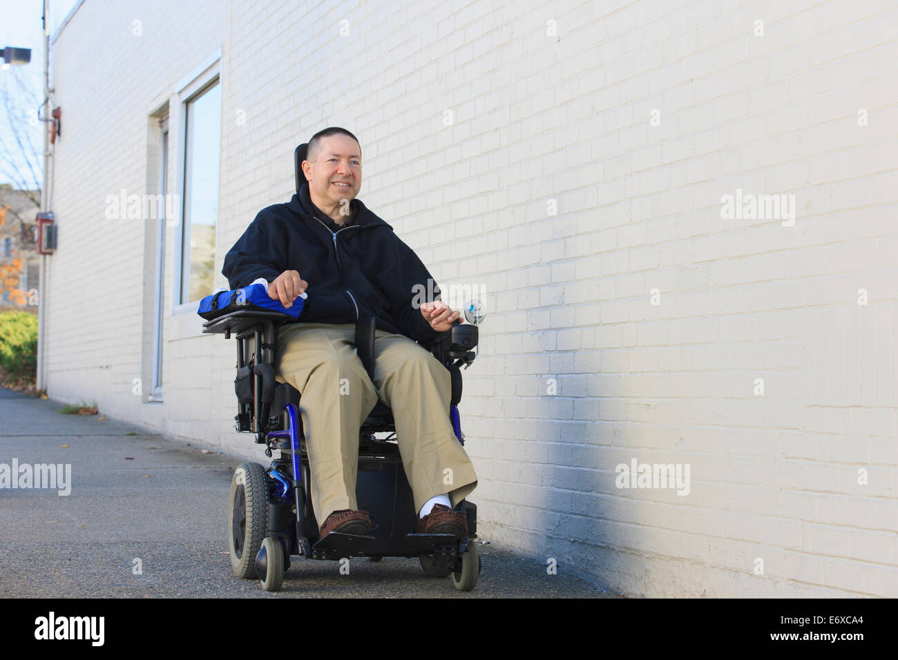 L'homme avec la moelle épinière et le bras de lésions nerveuses en fauteuil roulant motorisé à l'aide d'une rue publique Banque D'Images