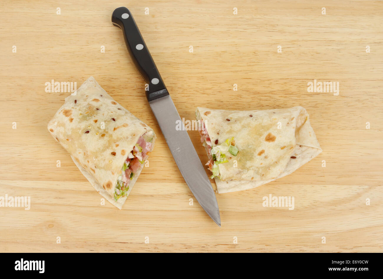 Couper le lard et de la salade pain wrap avec un couteau sur une planche en bois Banque D'Images