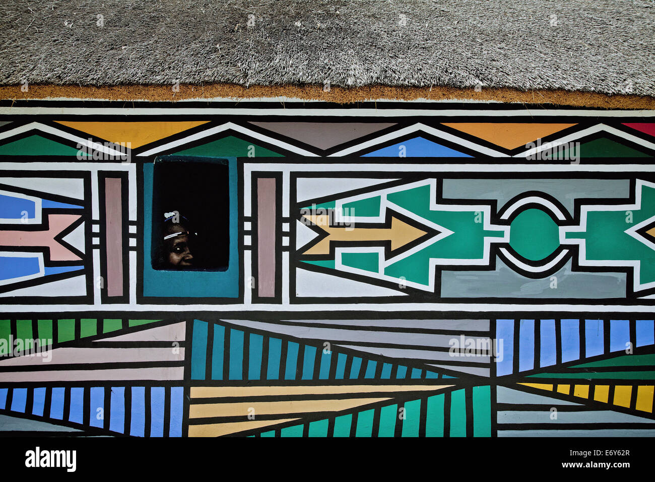 Femme de la tribu Ndebele regardant par une fenêtre de sa maison avec la façade traditionnelle peintures, Afrique du Sud, l'Afrique Banque D'Images