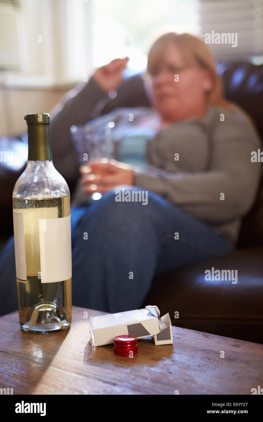 Femme assise sur un canapé avec une bouteille de vin et de cigarettes Banque D'Images