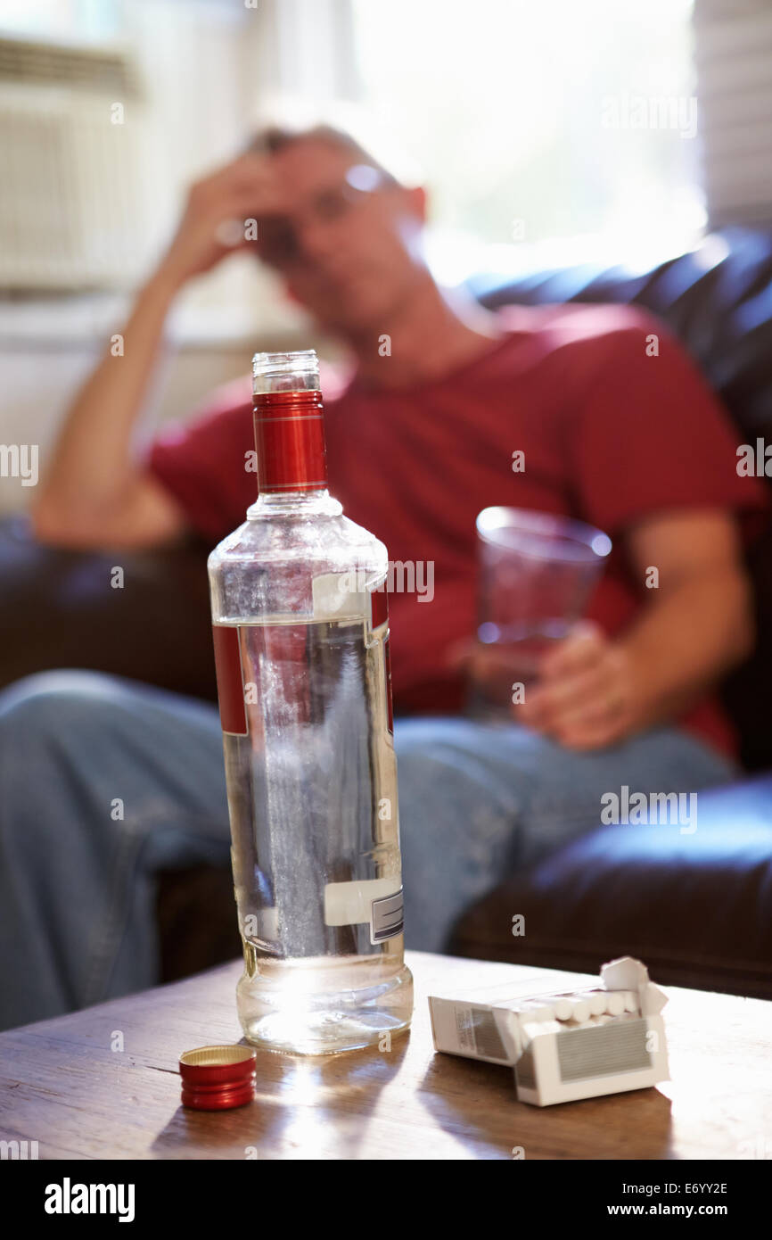 Homme assis sur un canapé avec une bouteille de vodka et de cigarettes Banque D'Images