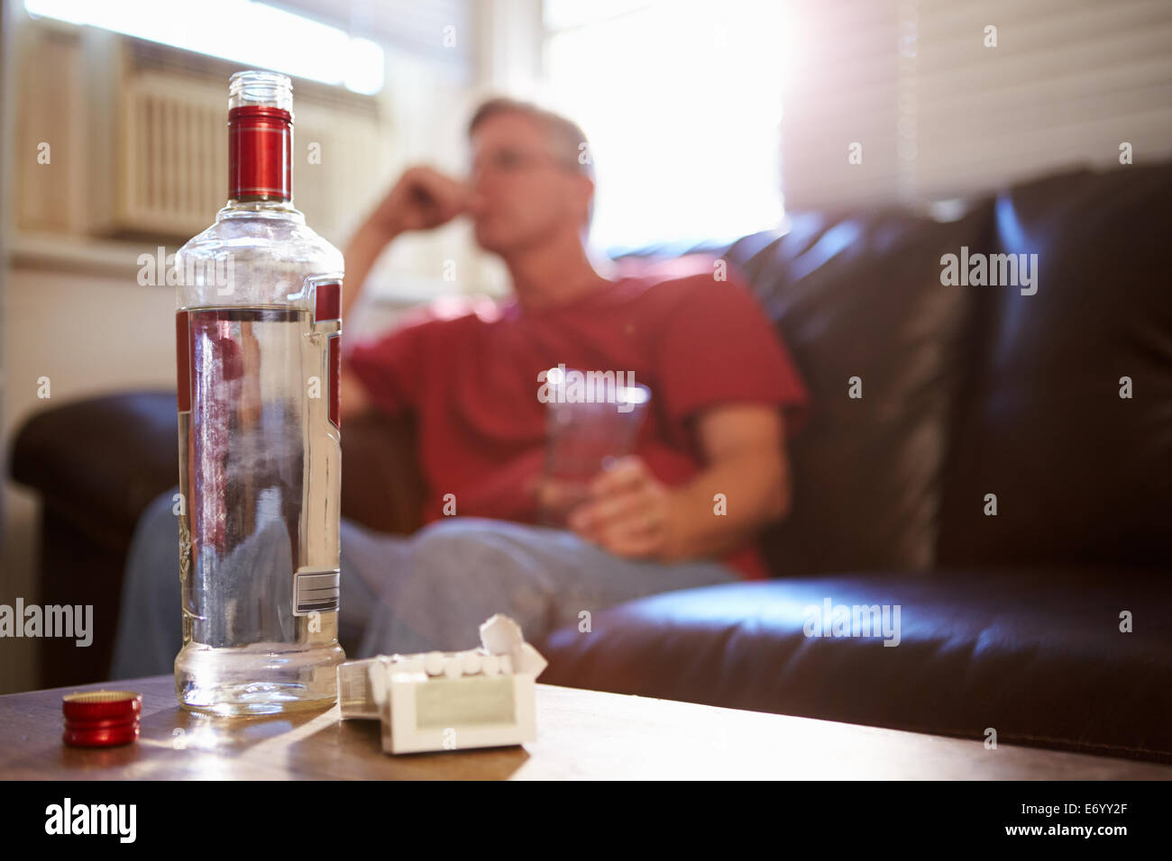 Homme assis sur un canapé avec une bouteille de vodka et de cigarettes Banque D'Images