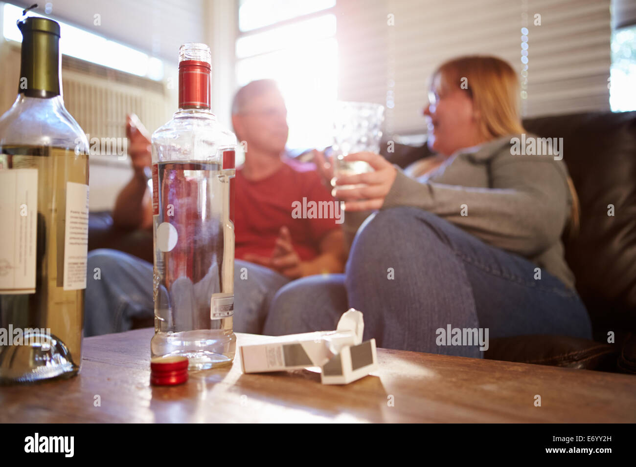 Couple assis sur le canapé avec une bouteille de vodka et de cigarettes Banque D'Images