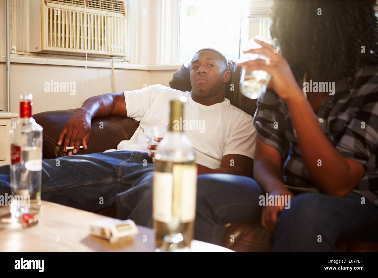 Couple assis sur le canapé avec une bouteille de vodka et de cigarettes Banque D'Images