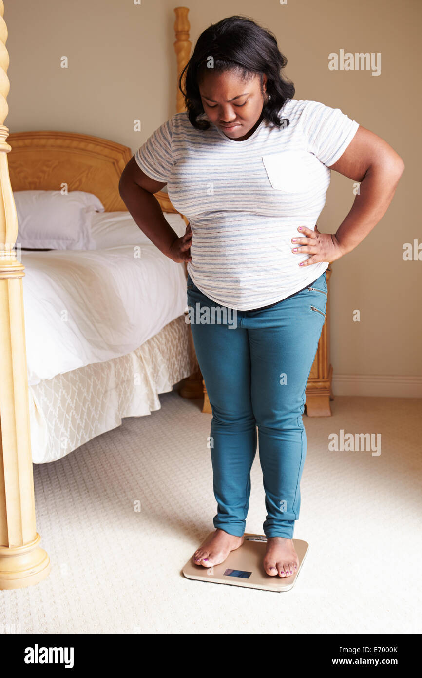Surpoids femme pesant elle-même à des échelles dans la chambre Banque D'Images