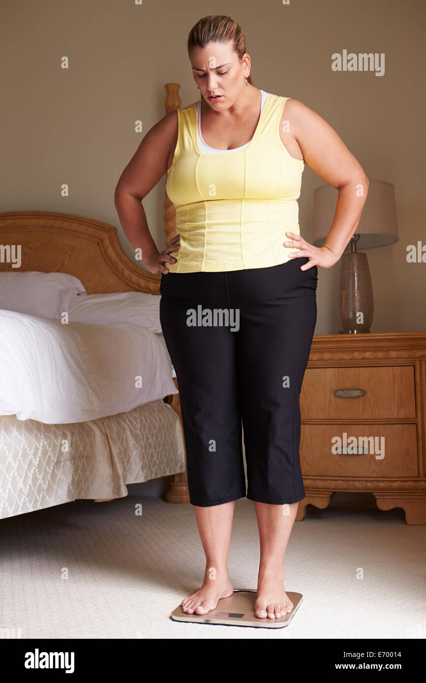 Surpoids femme pesant elle-même à des échelles dans la chambre Banque D'Images