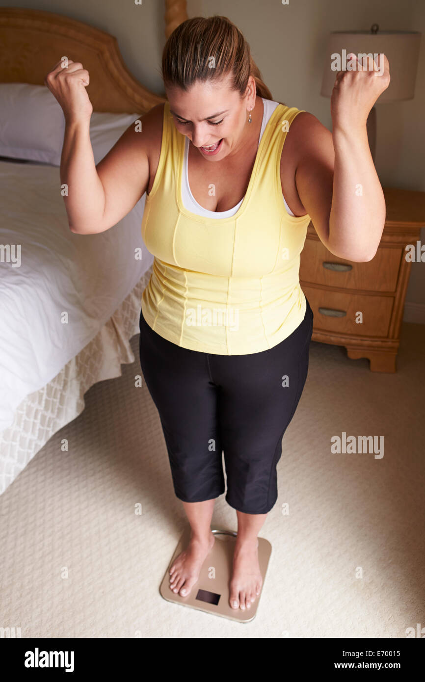 Surpoids femme pesant elle-même à des échelles dans la chambre Banque D'Images