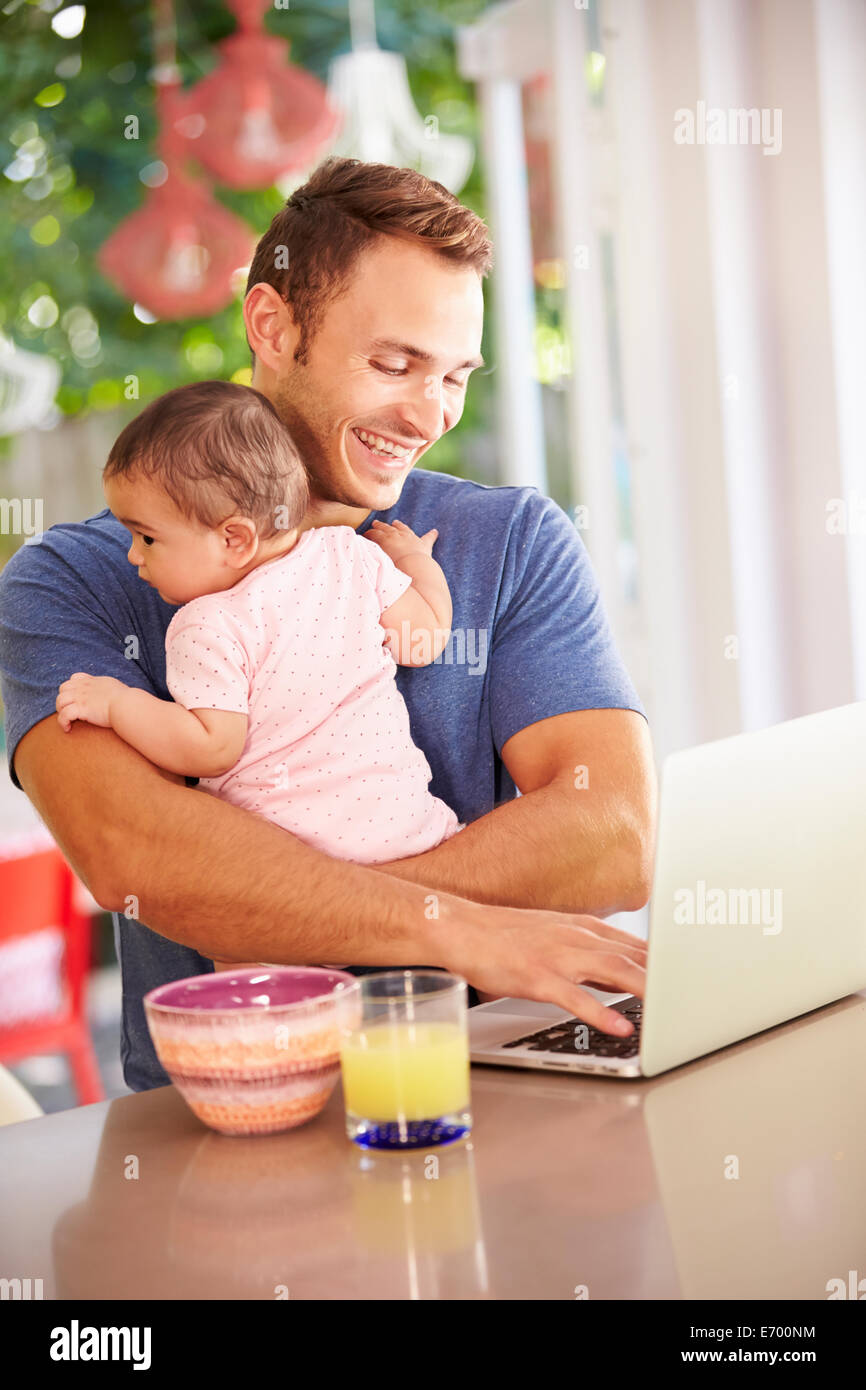 Père Holding Baby et faire collation tout en utilisant un ordinateur portable Banque D'Images