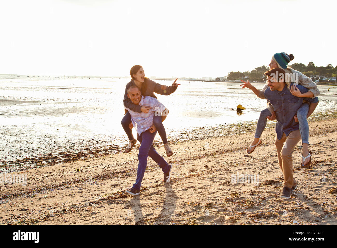Les hommes de donner aux femmes piggyback ride on beach Banque D'Images
