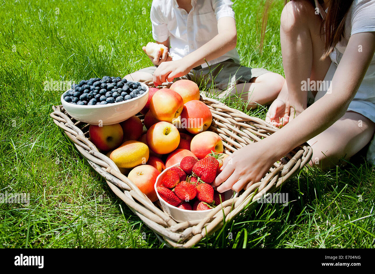 Portrait de frère et soeurs en mangeant des fruits de panier sur l'herbe Banque D'Images