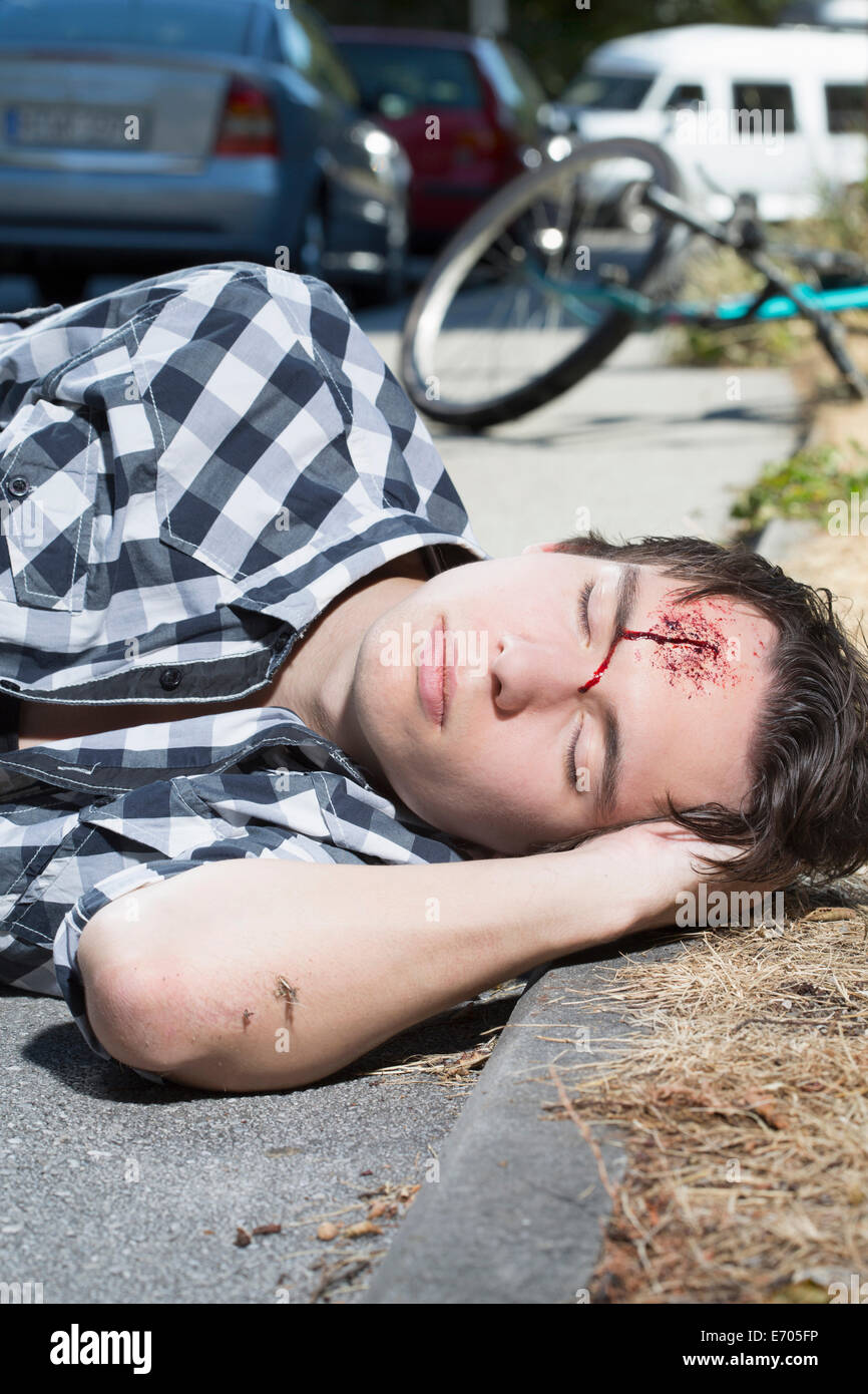 Jeune homme allongé sur la route avec saignement front Banque D'Images