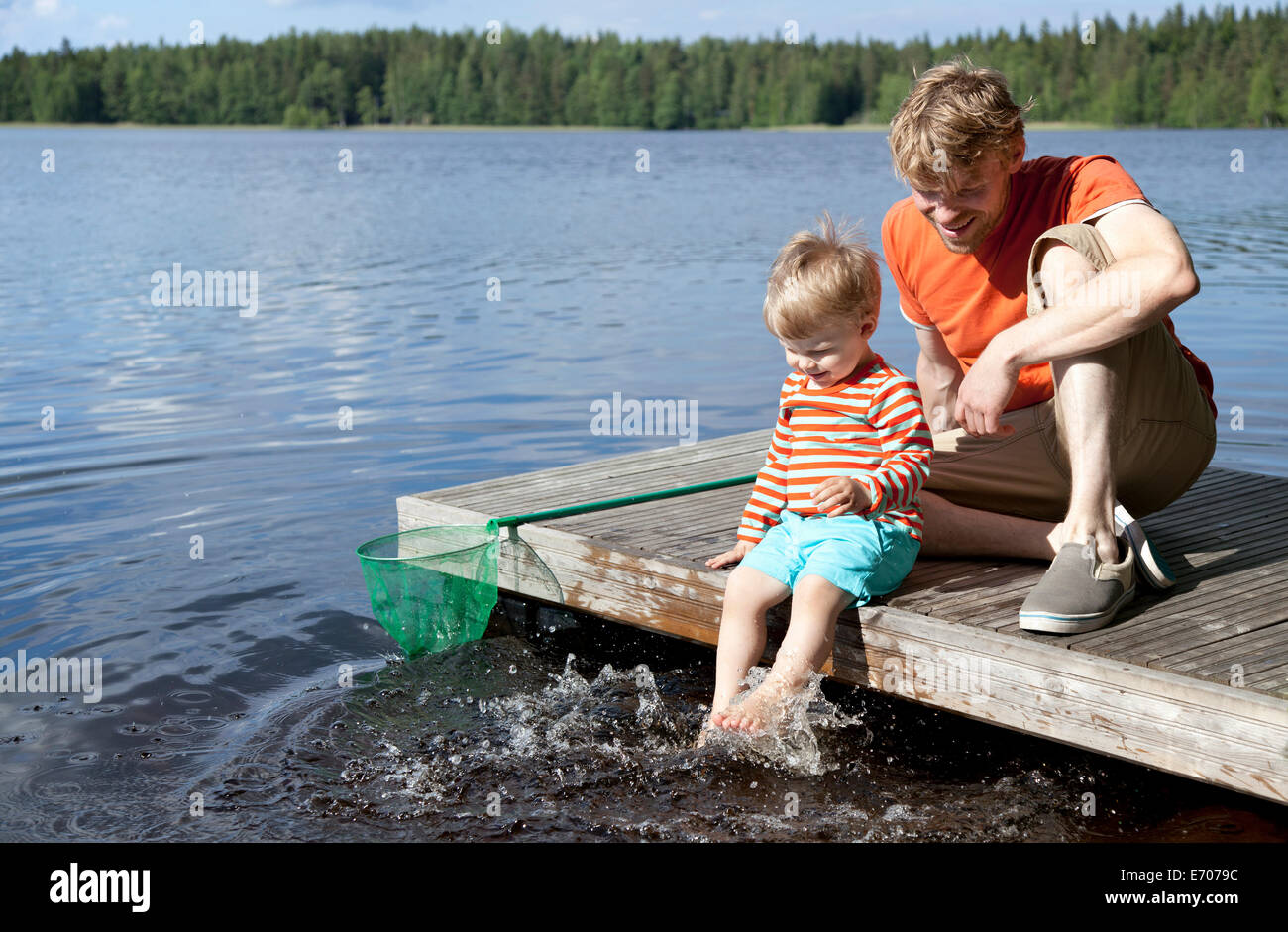 Père et fils assis sur la jetée du lac, Somerniemi, Finlande Banque D'Images