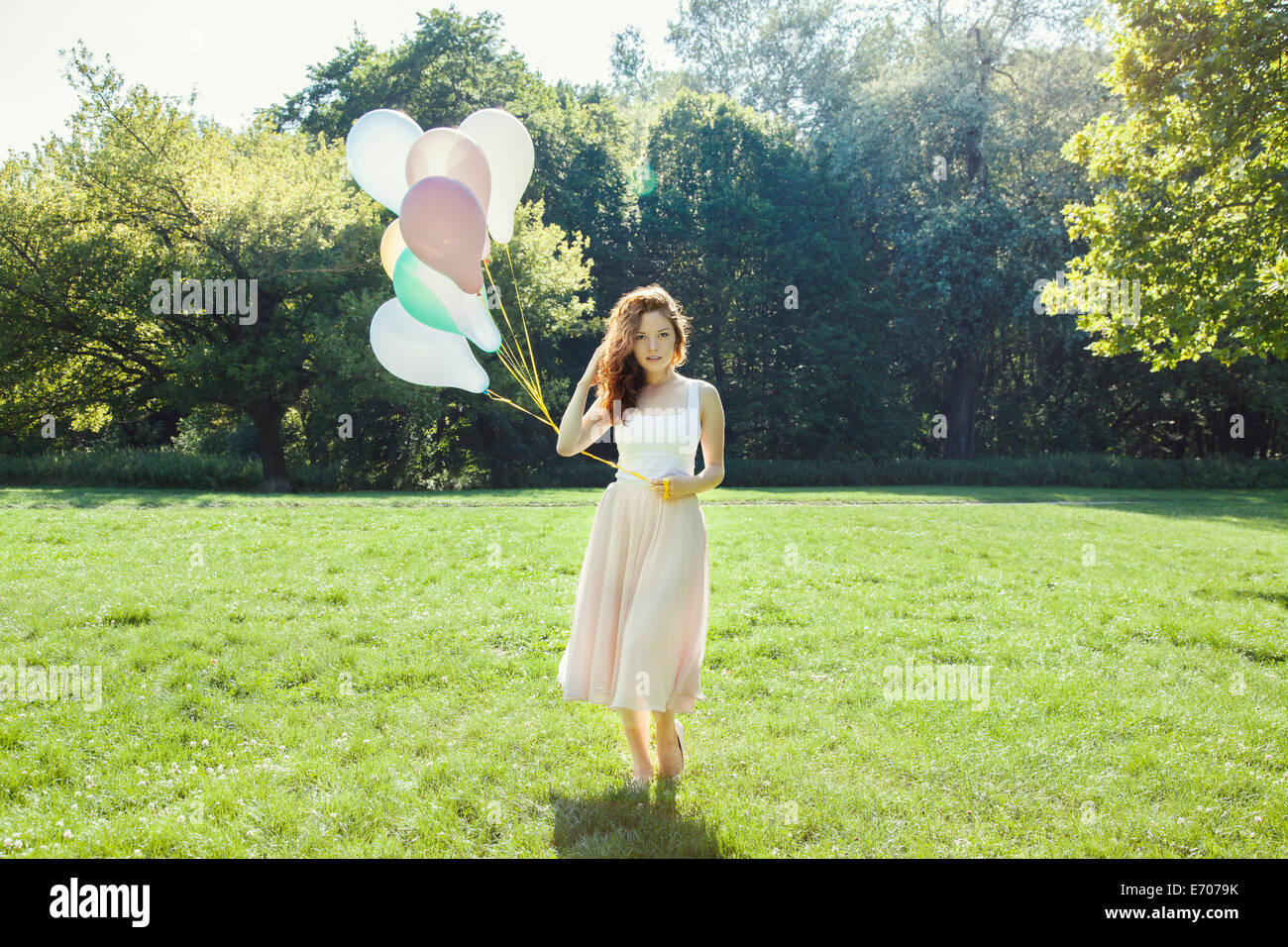 Portrait de jeune femme timide dans park holding a bunch of balloons Banque D'Images