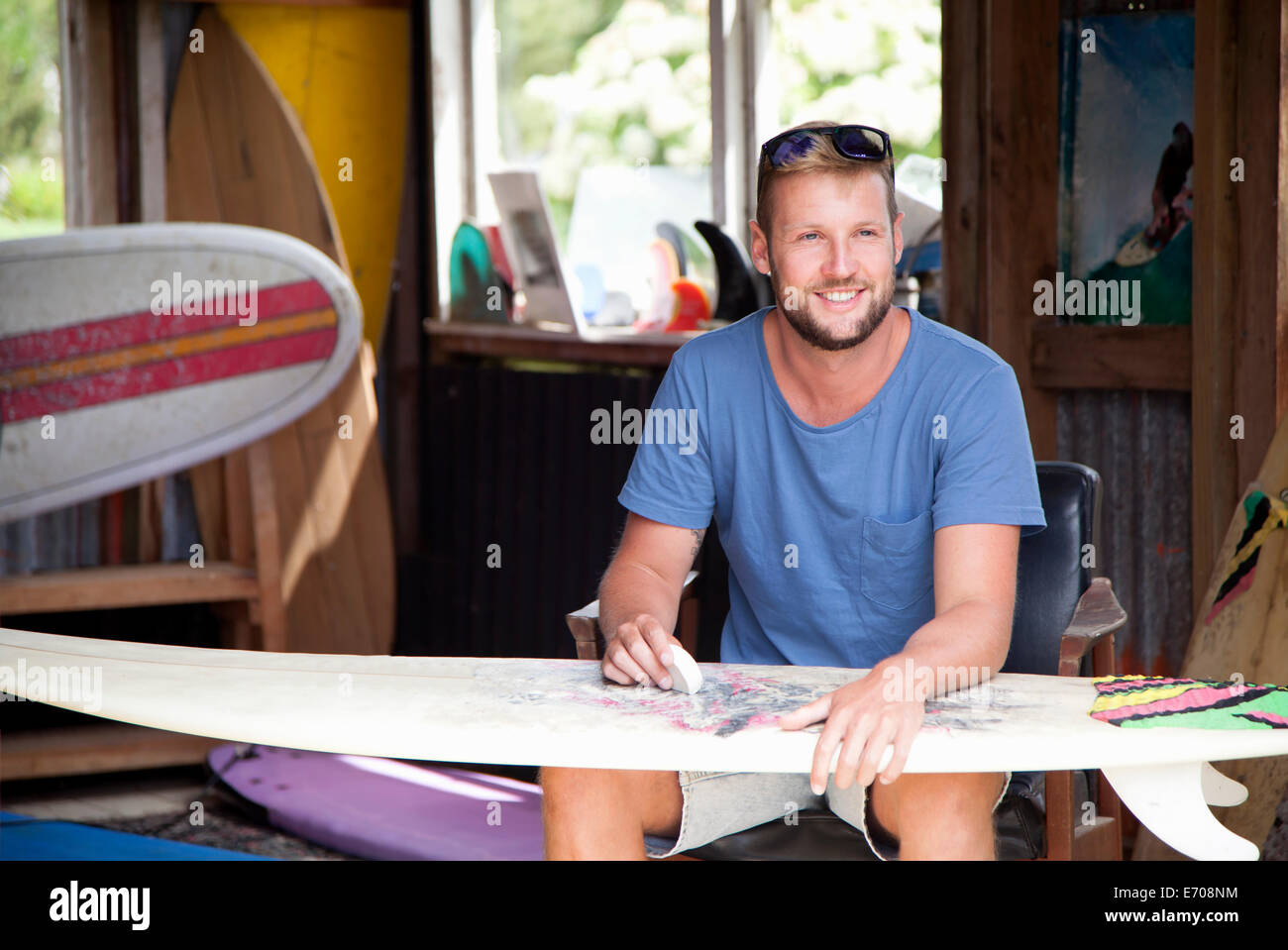 Young male surfer assis dans faire cirer his surfboard Banque D'Images