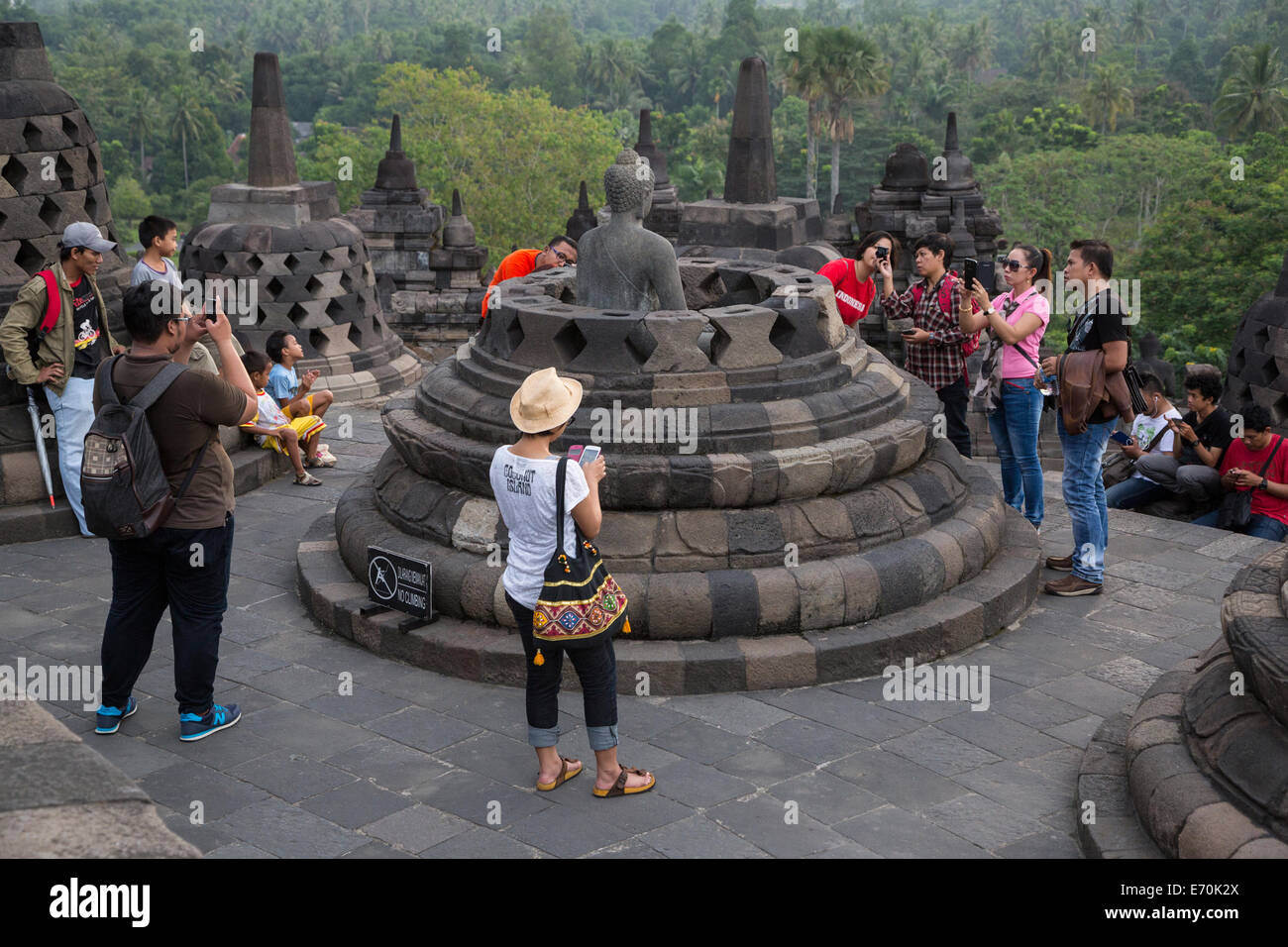 Borobudur, à Java, en Indonésie. Début de matinée les touristes réunis autour d'une statue de Bouddha dans un stupa. Banque D'Images
