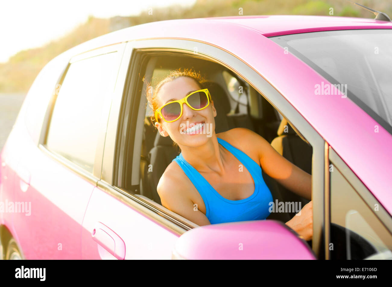 Belle jeune fille dans une voiture en souriant lunettes rose Banque D'Images