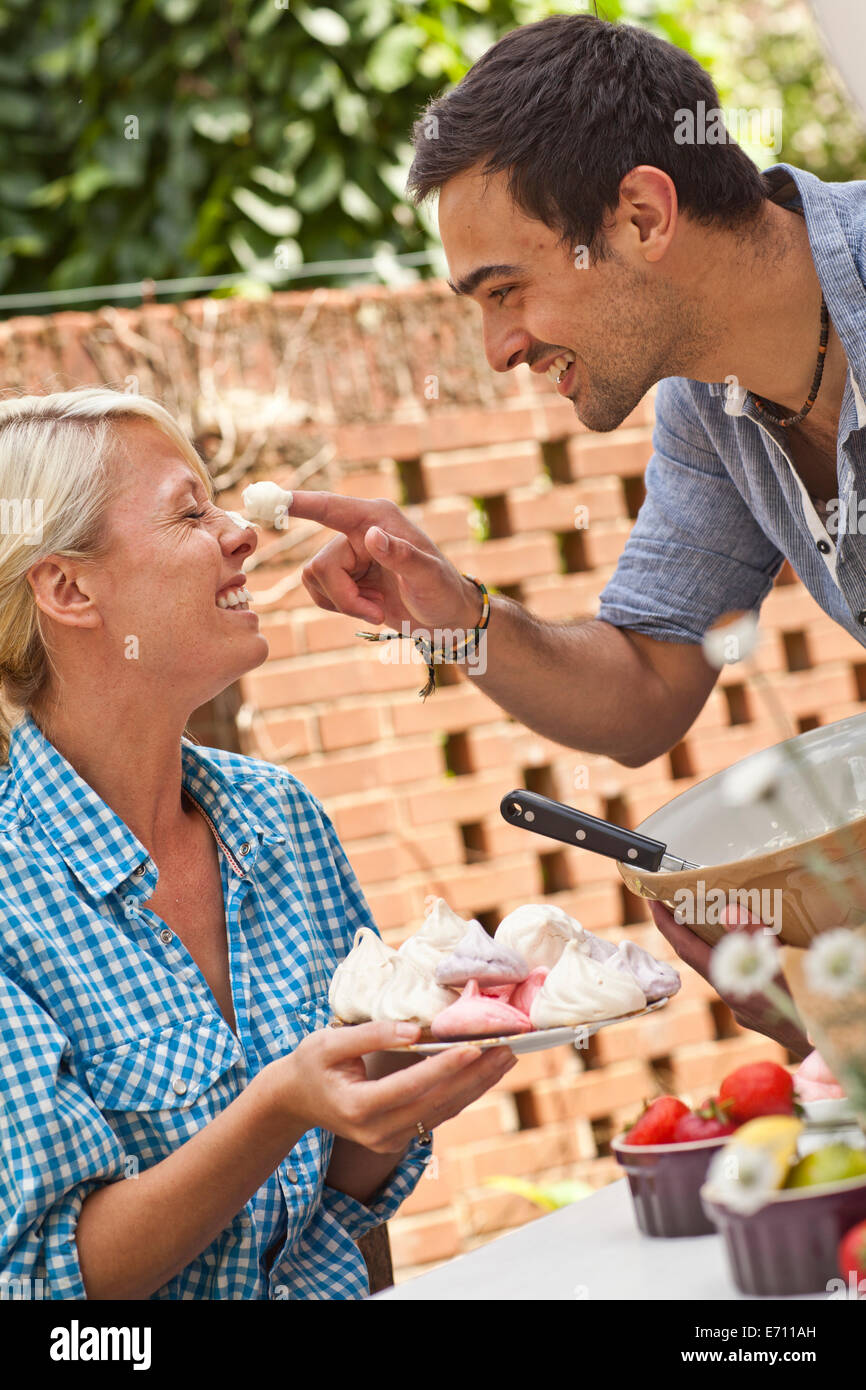 Jeune couple de jouer avec de la meringue at garden party Banque D'Images