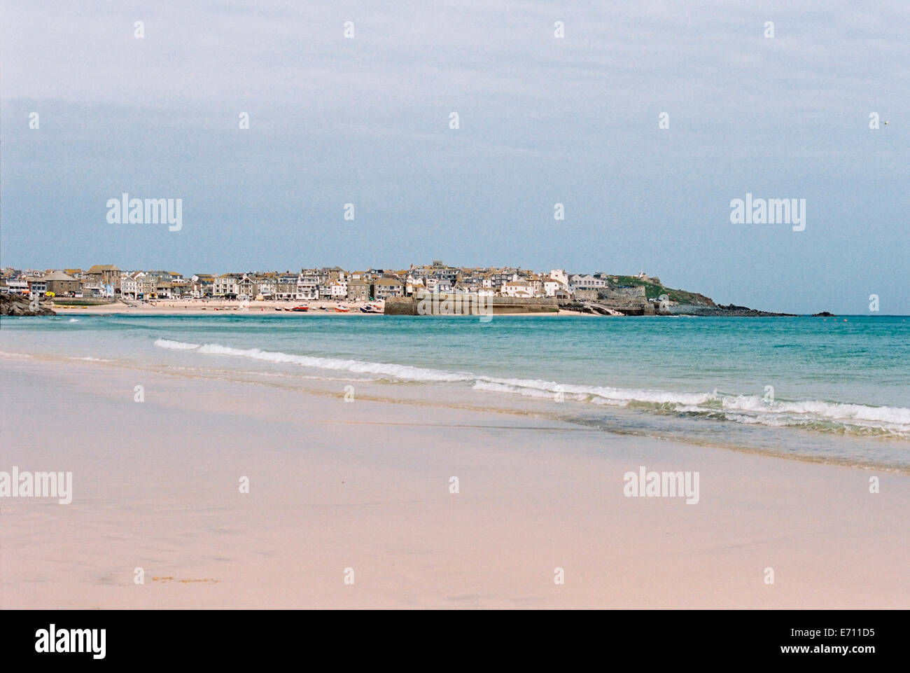 Un petit village sur un promontoire. Petites vagues se brisant sur le rivage d'une plage de sable avec une courbe lisse. Banque D'Images