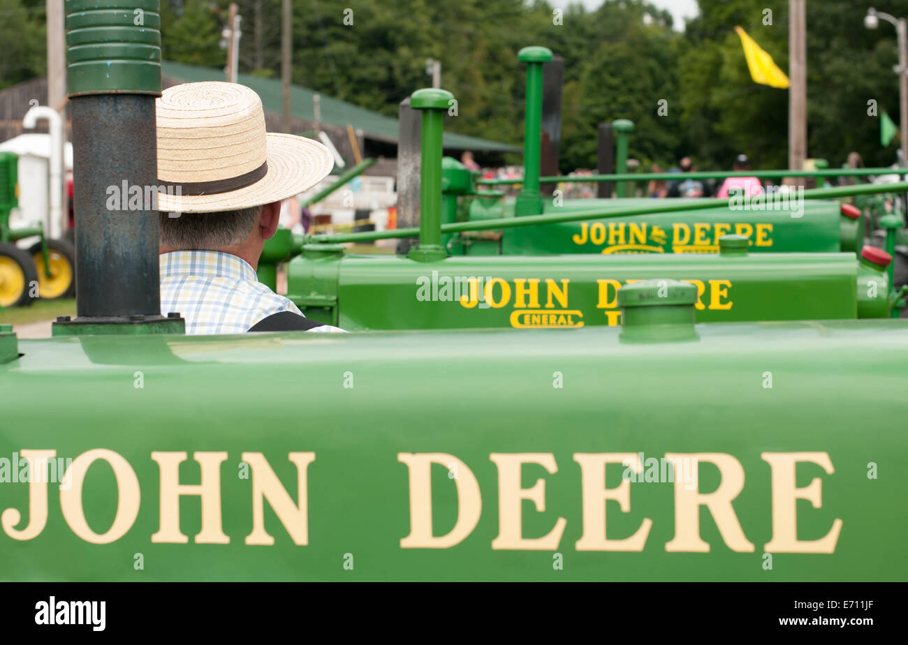 Un homme dans un chapeau de paille se trouve dans une rangée de tracteurs John Deere sur l'affichage à un tracteur John Deere à l'expo. Banque D'Images