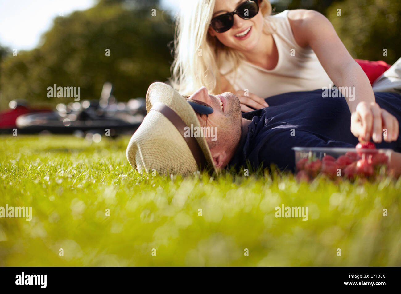 Jeune femme d'atteindre pour les fraises en petit ami couché dans park Banque D'Images