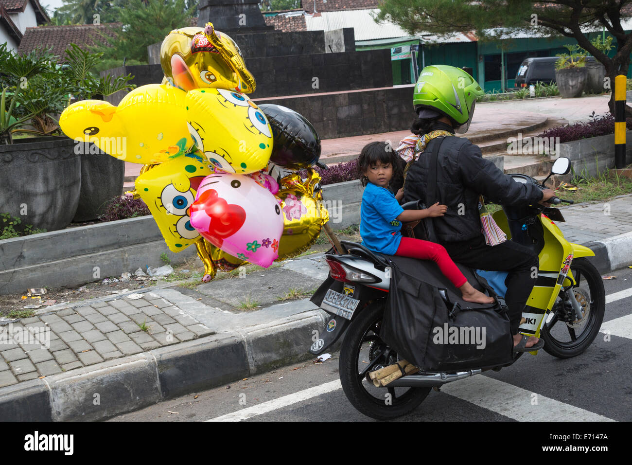 Yogyakarta, Java, Indonésie. La sécurité routière. Petite fille passe à la maison avec ses ballons, pas de casque. Banque D'Images