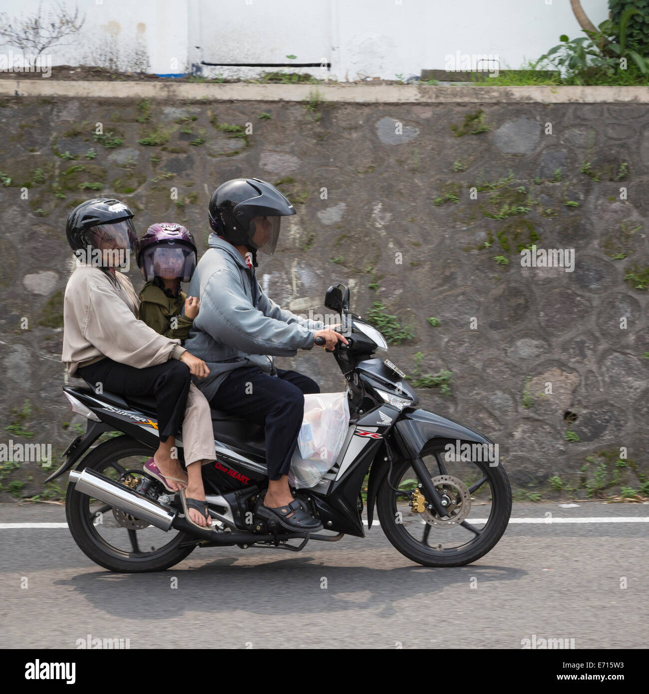 Yogyakarta, Java, Indonésie. La sécurité routière. Deux adultes et l'enfant sur une moto, le tout avec un casque. Banque D'Images