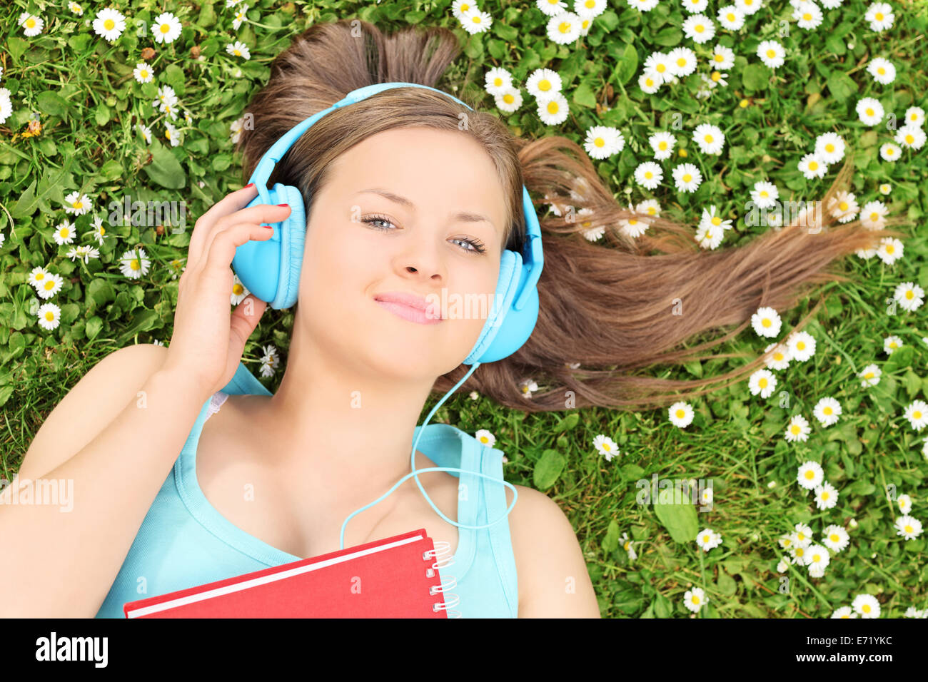 Belle jeune fille couchée dans un pré et listening to music on headphones Banque D'Images