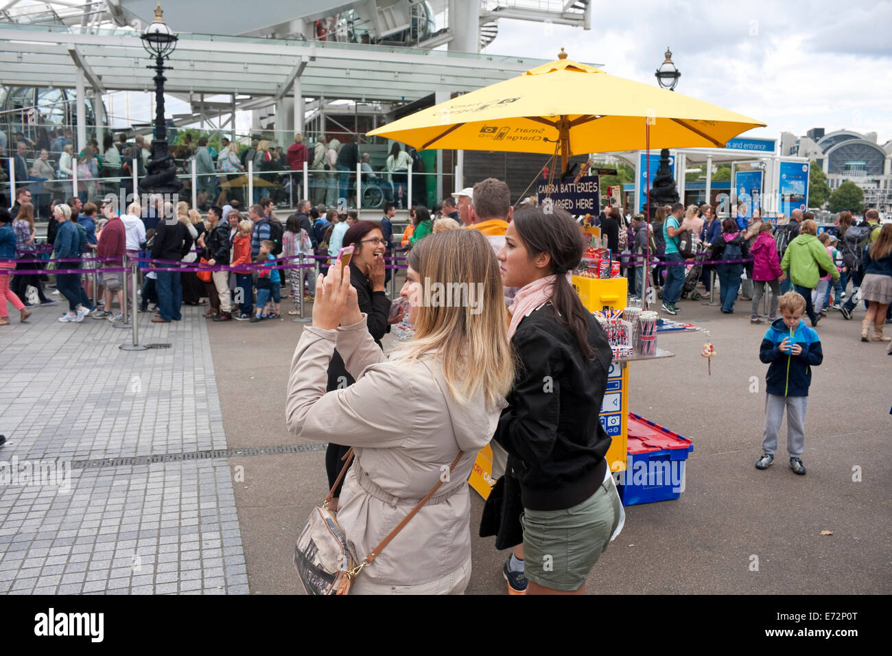 Deux jeunes femmes prenant des photos sur un téléphone intelligent à l'extérieur de l'Oeil de Londres, London, UK Banque D'Images