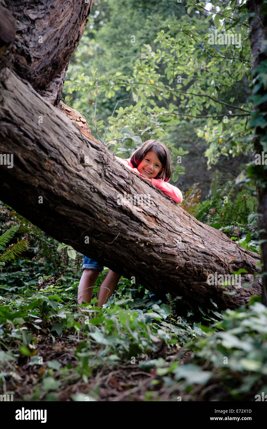 Portrait of smiling girl (6-7) leaning against tree trunk in forest Banque D'Images