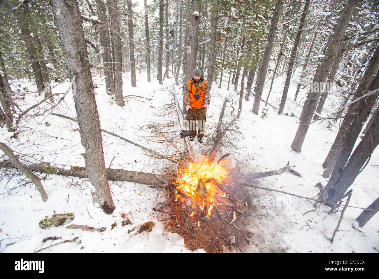 Un chasseur mâle reste chaud à côté d'un feu dans la neige. Banque D'Images