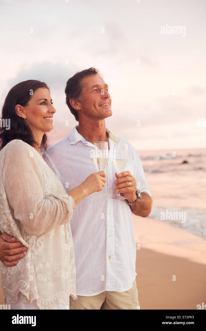 Happy Mature Couple Drinking Champagne sur la plage au coucher du soleil. Banque D'Images