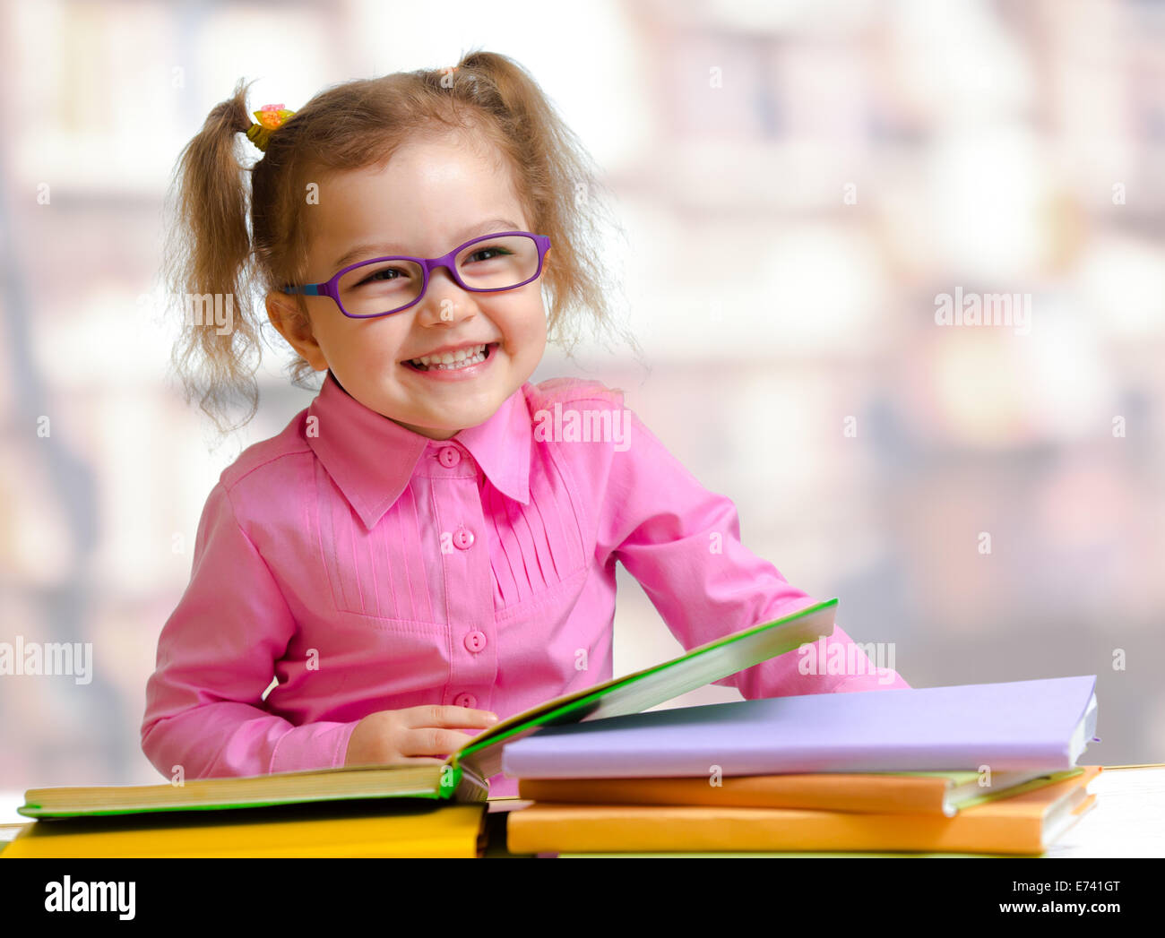 Happy child girl à lunettes la lecture de livres sitting at table Banque D'Images