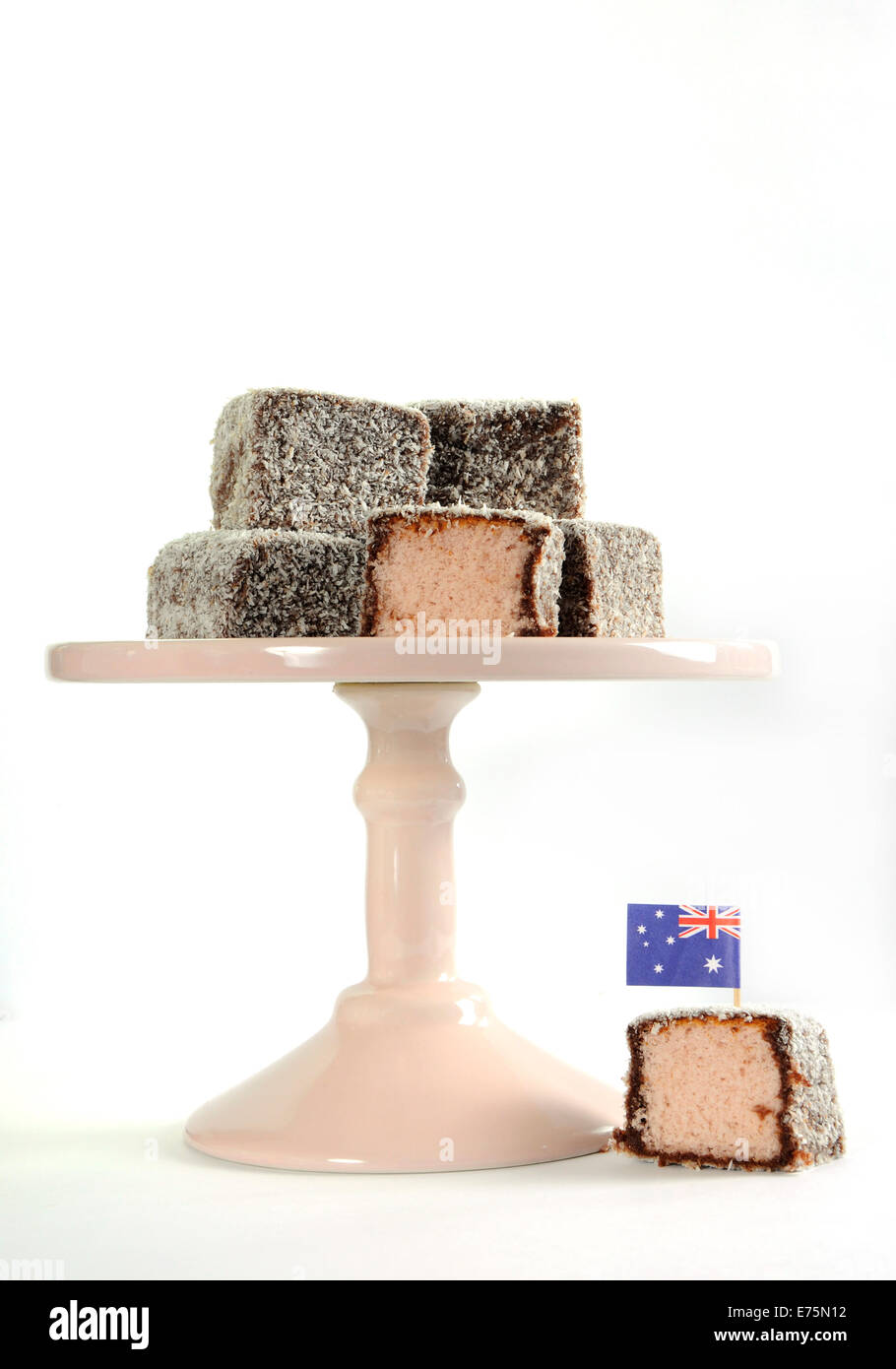 Gâteau traditionnel Australien, Lamington, rose pâle sur cake stand contre un fond blanc. Banque D'Images