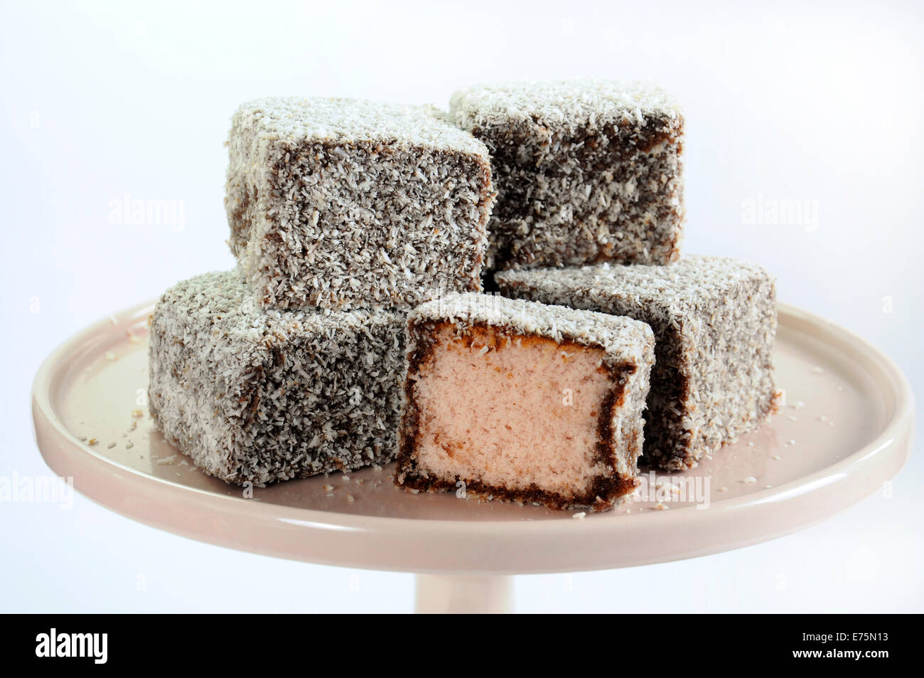 Gâteau traditionnel Australien, Lamington, rose pâle sur cake stand contre un fond blanc. Libre. Banque D'Images