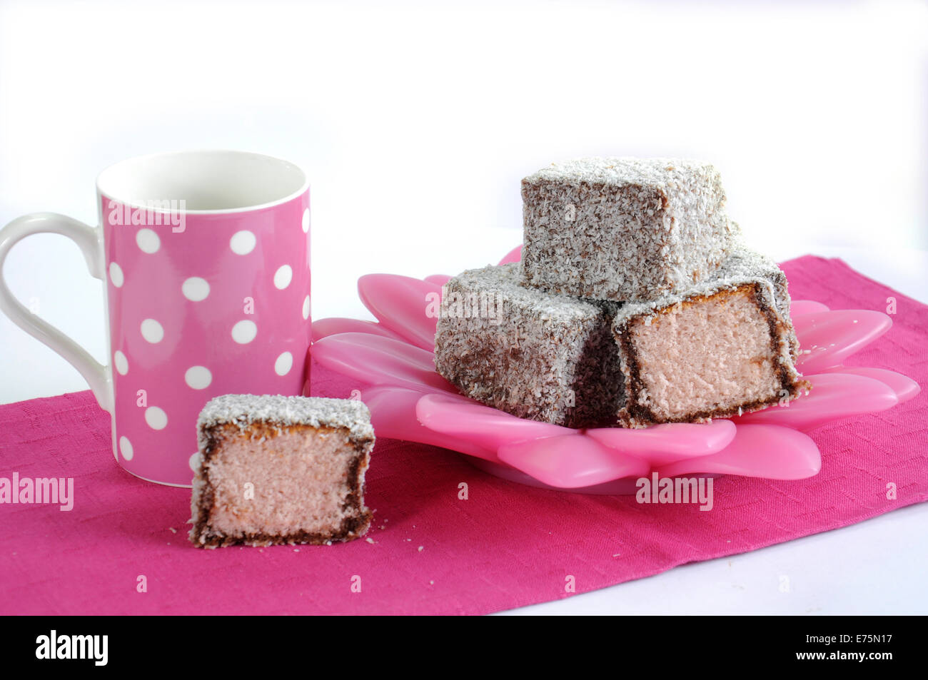 Gâteau traditionnel Australien, Lamington, sur plaque rose et blanc à pois rose avec serviette tasse de café sur un fond blanc. Banque D'Images